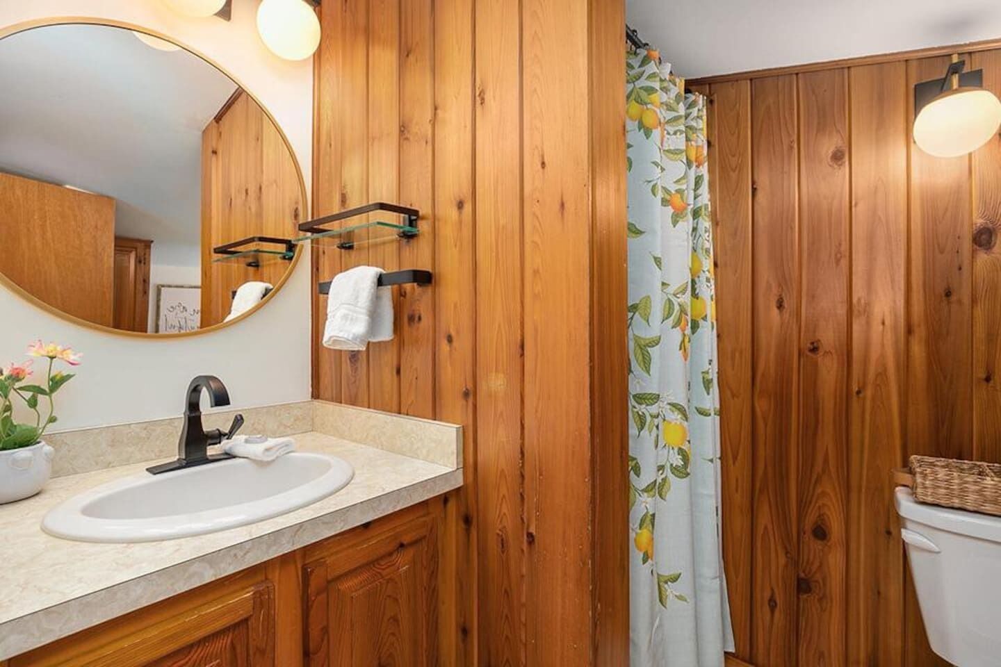 A wooden bathroom with a round mirror, a sink, and a toilet.