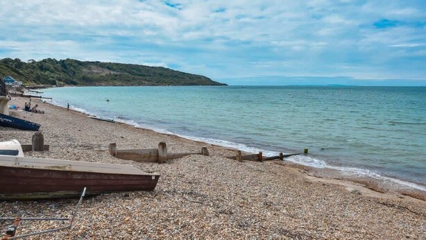 A pebble beach with boats, a wooden structure, and a distant hill. - Dartmouth House - Bayside (Totland Bay)