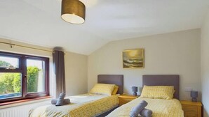 A room with two beds, a window with curtains, a painting on the wall, and a lamp on each bedside table. - Dartmouth House - Bayside (Totland Bay)