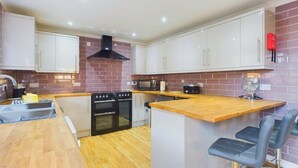 A modern kitchen with white cabinets, a brick backsplash, a central island with seating, and a built-in oven. - Dartmouth House - Bayside (Totland Bay)