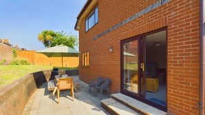 A brick building with a patio area featuring a wooden bench, a table, and chairs. - Dartmouth House - Bayside (Totland Bay)