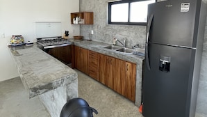 Une cuisine moderne dotée d’un plan de travail en marbre, de meubles en bois, d’un réfrigérateur noir et d’une fenêtre située au-dessus de l’évier.