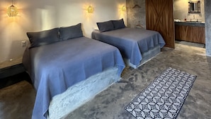Une chambre avec deux lits, un ventilateur de plafond et une petite kitchenette.
