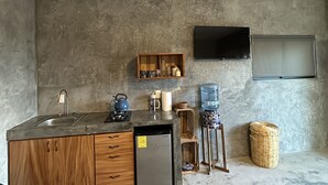 Une cuisine compacte dotée d’un évier encastré, d’un petit réfrigérateur, de meubles de rangement en bois et d’un distributeur d’eau.