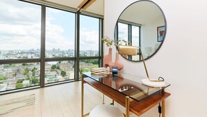 Un espace de bureau moderne avec un bureau en verre, un grand miroir rond et une vue sur le paysage urbain grâce à de larges fenêtres.