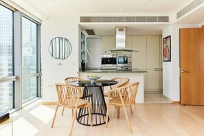 A modern kitchen with a central island, built-in oven, and microwave. There is a dining area with a round table and four chairs. - The Canary Wharf Place - Stunning 2bdr Flat (London)