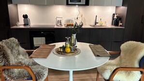 Una cocina moderna con una mesa blanca, dos sillas de piel, un tostador, un microondas y un lavabo.