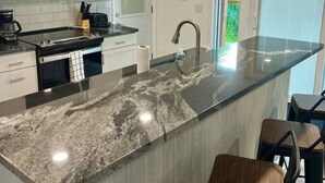 A modern kitchen with white cabinets, a granite countertop, and a built-in island with bar stools. - GOTL - Hot Tub - Wine Tours - Sunset Vacation Rentals (Geneva)