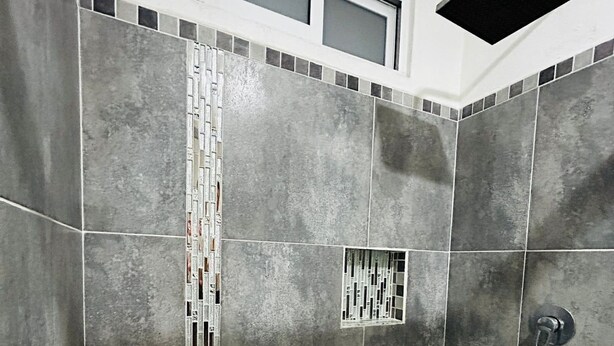 Un área de ducha con azulejos grises, piso a cuadros y una ventana pequeña en la parte superior.