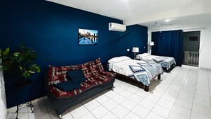 Camera d'albergo con due letti, un divano, una pianta in vaso e una fotografia con vista sulla città.