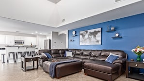 A modern living room with a sectional sofa, a dining area, and a kitchen in the background. - Aris Oasis  Private Pool Heat Included (Gilbert)