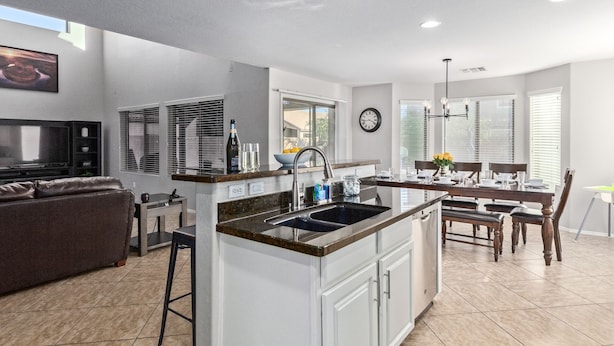 A modern kitchen with a central island, a dining area with a chandelier, and a living room with a TV and seating. - Aris Oasis  Private Pool Heat Included (Gilbert)