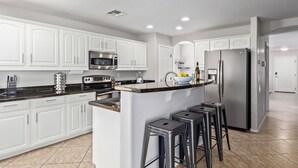 A modern kitchen with white cabinetry, stainless steel appliances, and a central island with bar stools. - Aris Oasis  Private Pool Heat Included (Gilbert)
