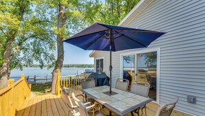 A wooden deck with a table and chairs, a blue umbrella, and a view of a lake. - Waterfront Lodi Vacation Rental on Lake Wisconsin! (Lodi)