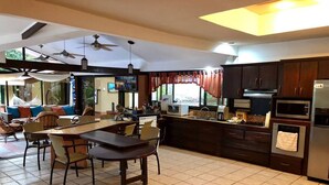A modern kitchen with dark wooden cabinets, a central island with seating, and a dining area with chairs. - Paradise Found!  Spacious Tropical Private Retreat! (Jaco)
