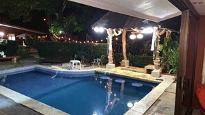 A swimming pool with a tiled edge, surrounded by a covered patio area with string lights. - Paradise Found!  Spacious Tropical Private Retreat! (Jaco)