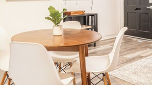 Un comedor con una mesa redonda de madera, sillas blancas, una planta en maceta y cuadros en la pared.