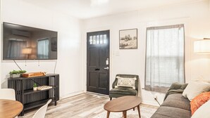 Una sala de estar con una puerta negra, un televisor de pantalla plana, un sillón verde, un sofá marrón y una mesa de centro de madera.
