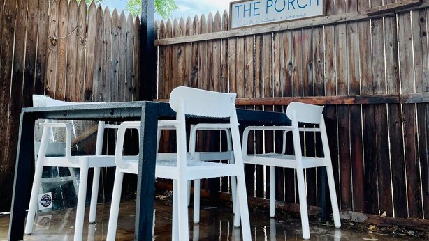 A covered outdoor seating area with a wooden fence, a sign reading "THE PORCH," and string lights. - This house is a 2 bedroom(s), 1 bathrooms, located in Abilene, TX. (Abilene)