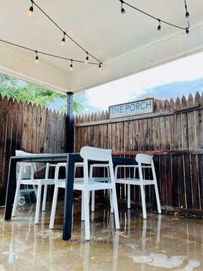 A covered outdoor seating area with a wooden fence, a sign reading "THE PORCH," and string lights. - This house is a 2 bedroom(s), 1 bathrooms, located in Abilene, TX. (Abilene)