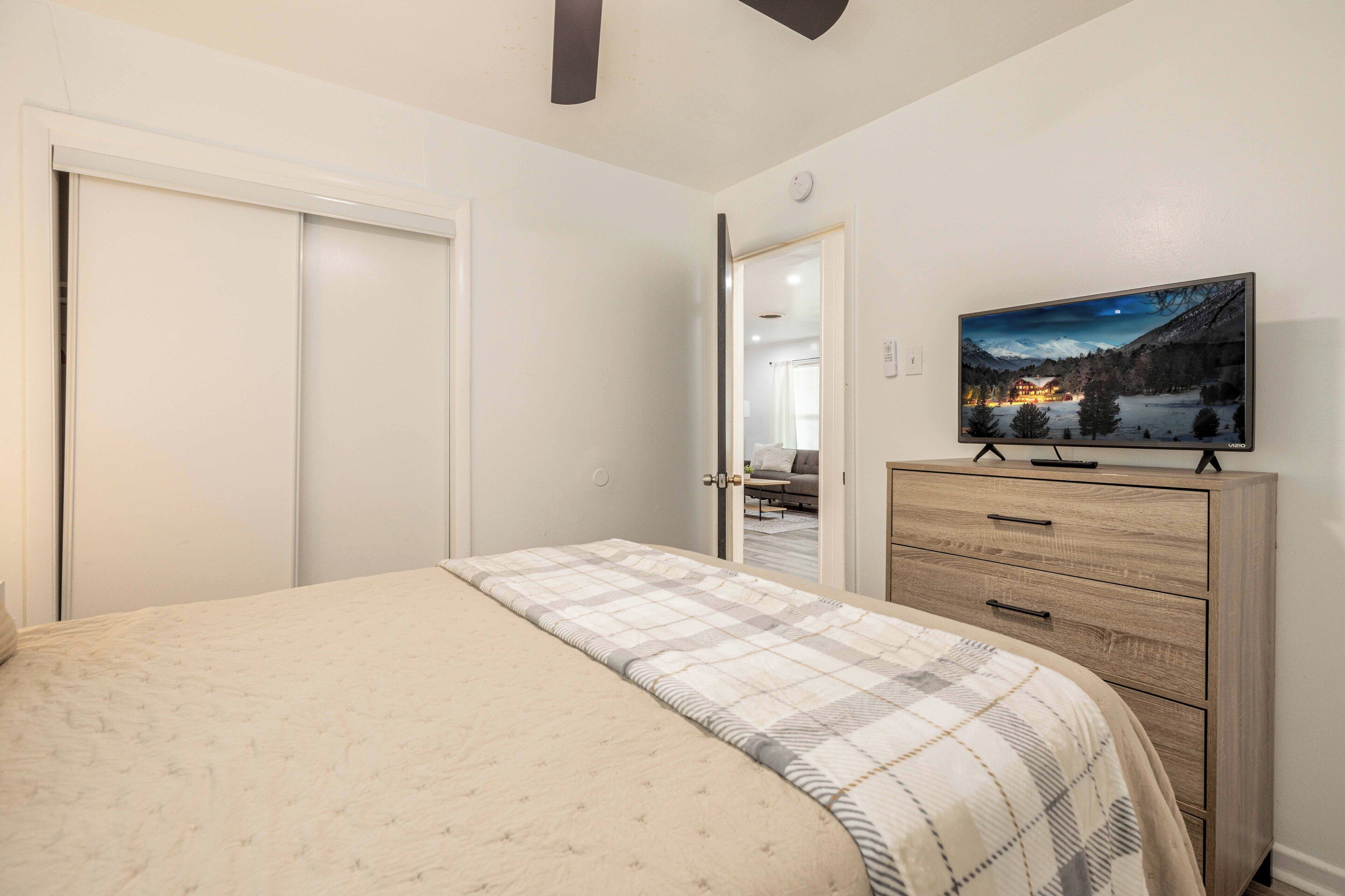 A bedroom with a bed, a wooden dresser, and a TV on a stand.