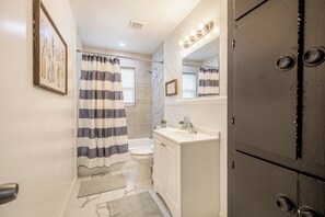 A bathroom with a shower, toilet, and sink, featuring a striped shower curtain and a mirror with lights. - Cut the claustrophobia in hotels, enjoy freedom and quality space. (Abilene)