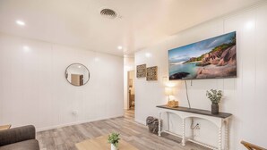 A modern living room with a wooden coffee table, a sofa, a round mirror, and a large painting of a coastal scene. - Cut the claustrophobia in hotels, enjoy freedom and quality space. (Abilene)