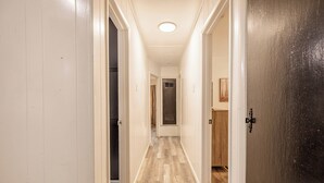 A narrow hallway with wooden flooring, white walls, and a door with a black panel on the right. - Cut the claustrophobia in hotels, enjoy freedom and quality space. (Abilene)