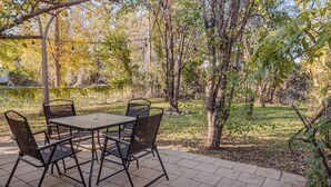Eine Terrasse im Freien mit Tisch und vier Stühlen, umgeben von Bäumen und einer Rasenfläche.