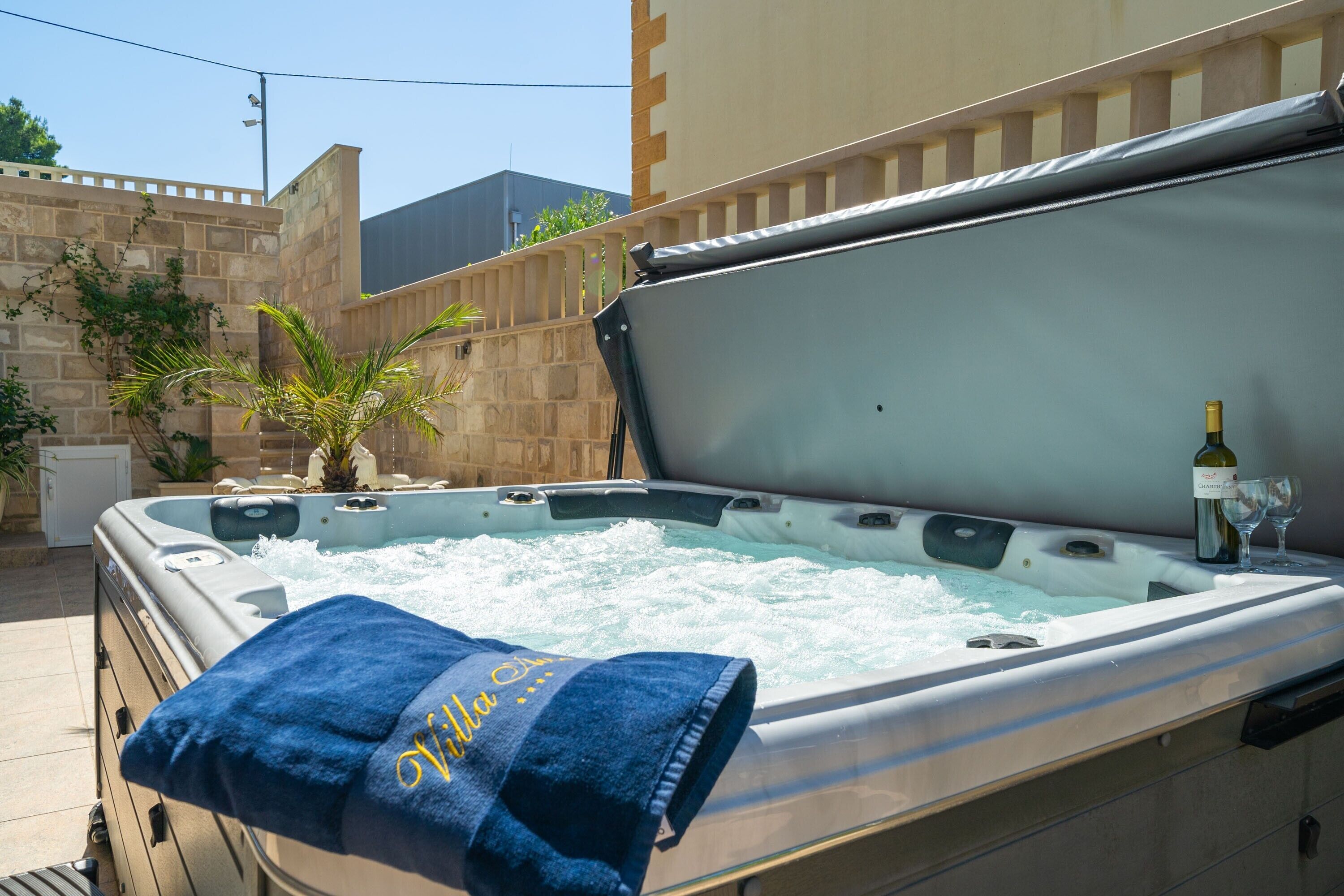 Un bain à remous avec une serviette et une bouteille de vin, entouré d’un mur de pierres et de plantes.