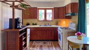A compact kitchen with wooden cabinets, a gas stove, a coffee machine, and a window with a view of greenery outside. - The Gemini (Elkhart)