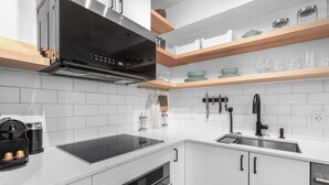 Une cuisine moderne avec des armoires blanches, une cuisinière noire et des étagères en bois au-dessus du plan de travail.