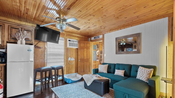 A cozy cabin-style room with a wooden ceiling, a green sofa, a small kitchen area, and a pet bed.
