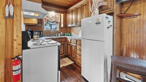A kitchen with wooden cabinets, a white refrigerator, a stove, and a fire extinguisher.