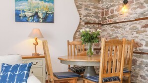 A dining area with a stone wall, a table with chairs, a lamp, and a painting of boats. - Baronet's Quarters (Lynton)