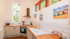 A modern kitchen with wooden countertops, a built-in oven, and a window with a view of greenery. - Baronet's Quarters (Lynton)