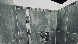 Ein kleines Duschbad mit gefliesten Wänden und einem Schachbrettmuster Boden, inklusive Abfluss.