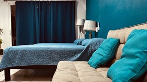 Ein Hotelzimmer mit einem beigen Sofa, einer blauen Bettdecke und einem Deckenventilator.