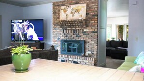 A living room with a brick fireplace, a television, and a green plant. - Lake Oasis w/Pool, Hot tub, Gym (Warr Acres)