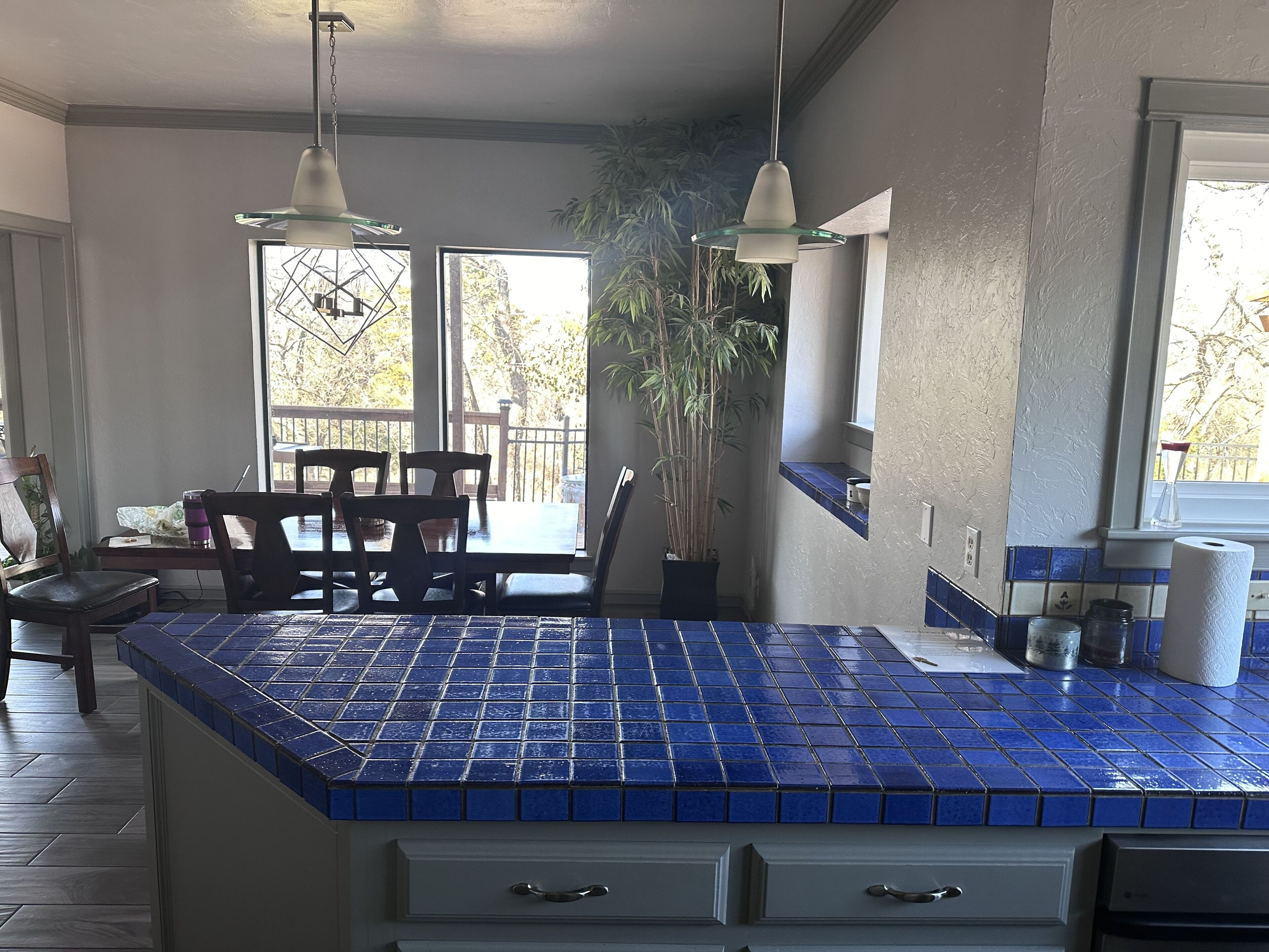 A kitchen with blue-tiled countertops, a dining area with wooden chairs, and a potted plant.