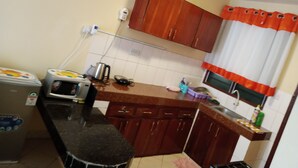 Eine kleine Küche mit Holzschränken, einer schwarzen Arbeitsplatte, einem Wasserkocher, einem Toaster und einem Fenster mit orangenen Vorhängen.
