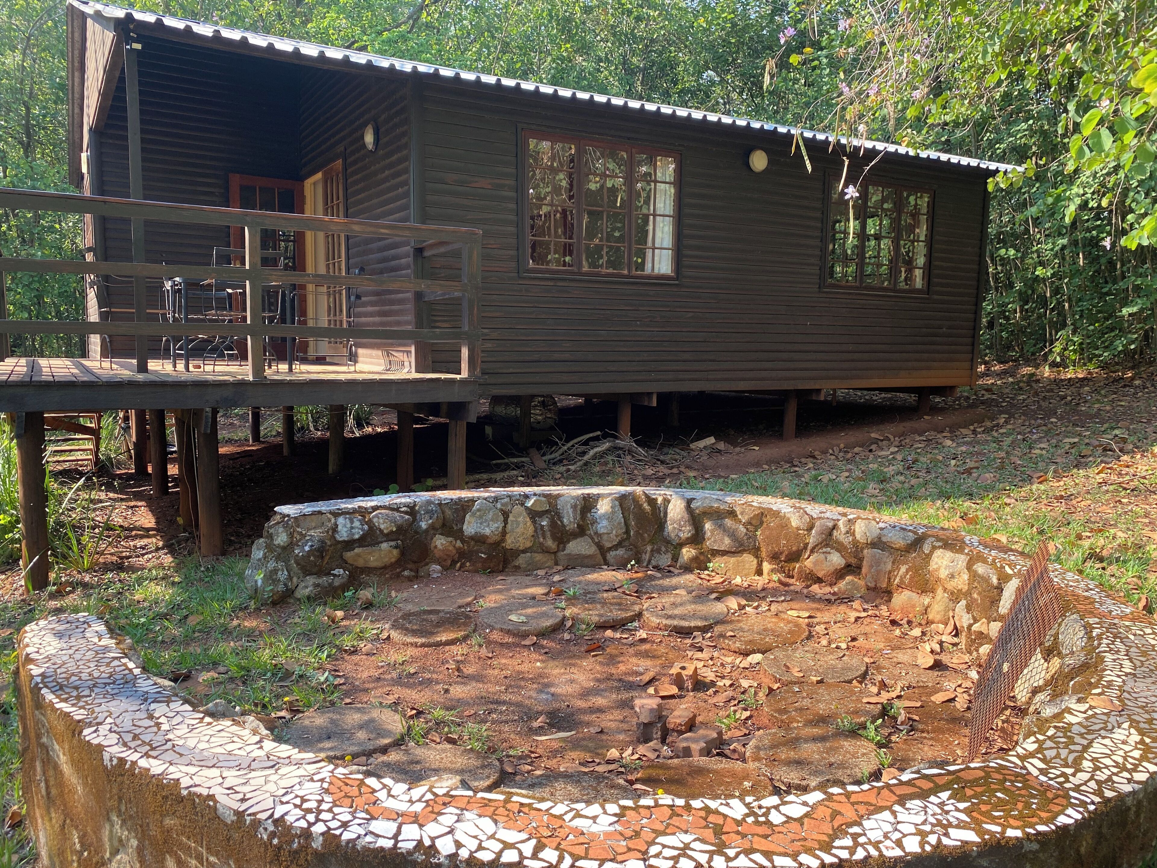 Una cabaña rústica con una terraza de madera y una fuente de agua con mosaicos de piedra.