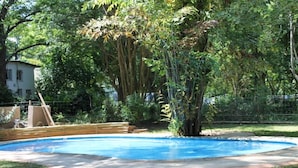 A swimming pool surrounded by lush greenery and a wooden deck. - Buhleni Farm & Chalets (Lobamba)