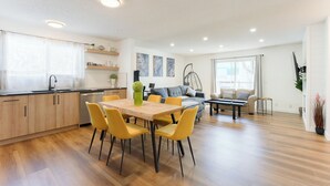 Eine moderne Küche mit Holzausstattung, einem Esstisch mit gelben Stühlen, einem grauen Sofa und einem Hängekorbstuhl.
