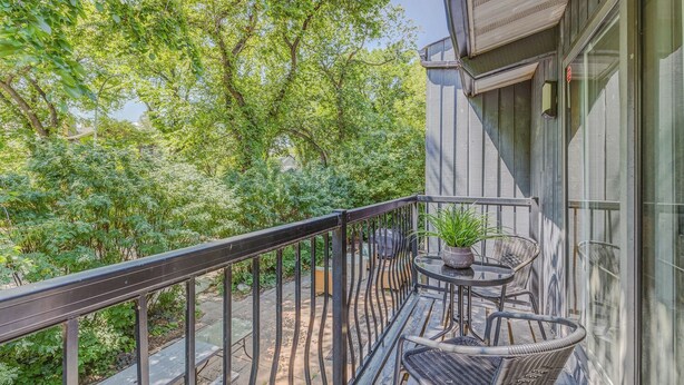 Ein Balkon mit schwarzem Geländer, einem kleinen runden Tisch mit einem Blumentopf und einem Korbstuhl.