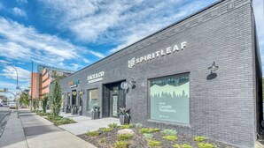 Ein Gebäude mit Ziegel Fassade, darunter Geschäfte wie 'Spiritleaf' und 'Beef'n'Broccoli, sowie ein Fenster mit Werbung für Cannabis.