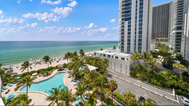 A resort with a pool, palm trees, and a view of the ocean. - Luxe Oceanfront Condo in Hollywood Beach (Hollywood)