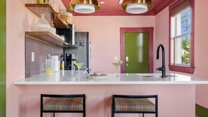 A kitchen with a white countertop, two black chairs, a green door, and a window with a view. - The Leo | In the Heart of Park Circle Main Strip (North Charleston)