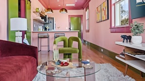 A modern living room with a glass coffee table, a red sofa, and a green armchair. - The Leo | In the Heart of Park Circle Main Strip (North Charleston)