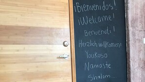 Una puerta de madera con una pizarra que muestra mensajes de bienvenida en varios idiomas.